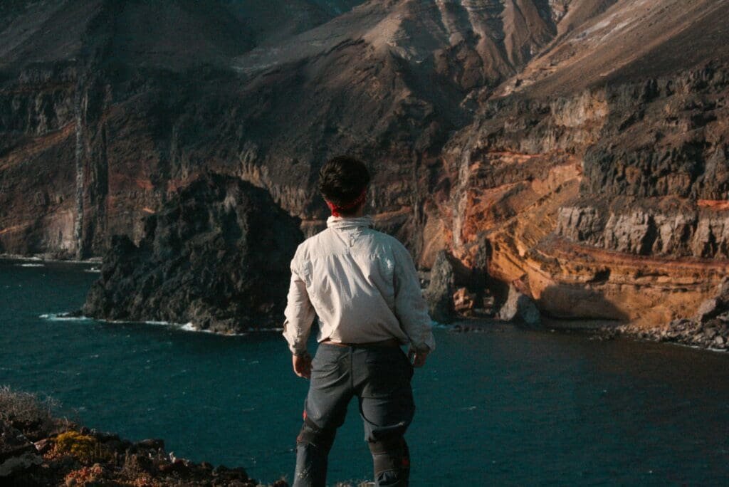 Traveler standing at a cliff edge overlooking a dramatic landscape, symbolizing suspense and anticipation.