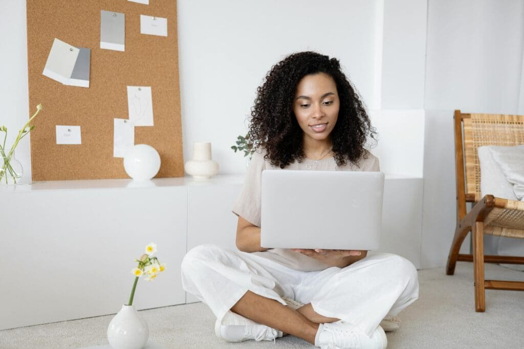 Woman sitting cross-legged on the floor using a laptop to plan her travel diary series.