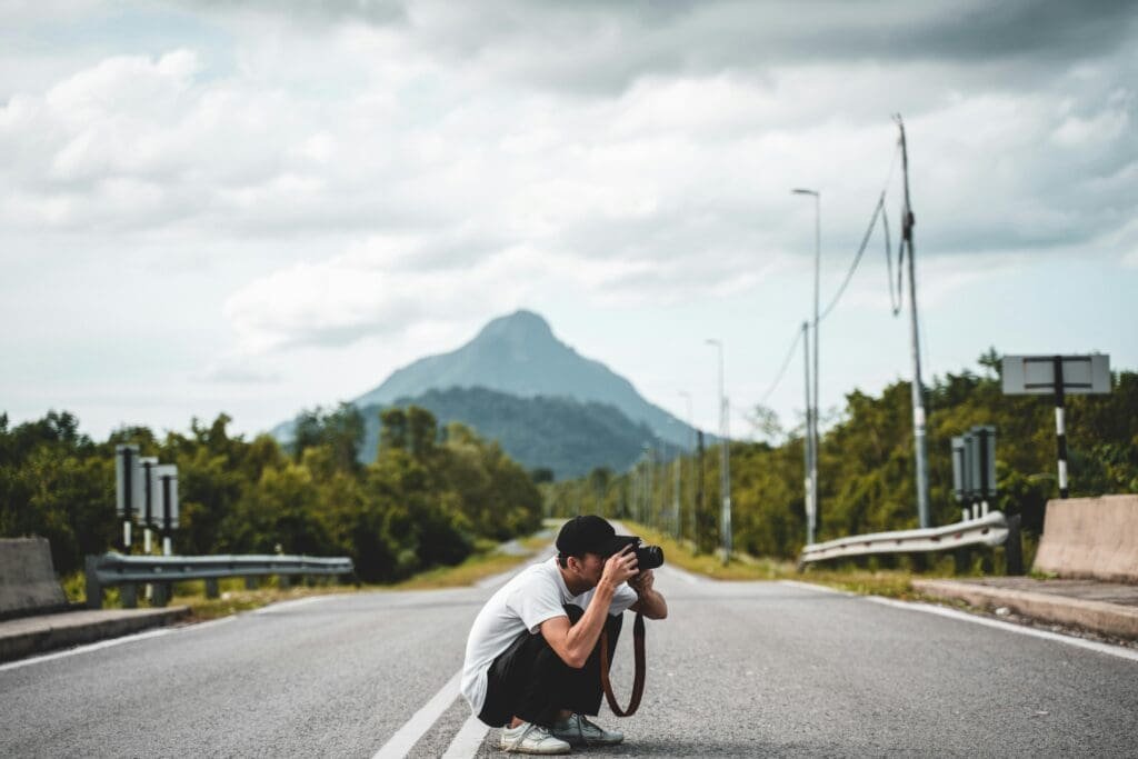 A man sitting on the road taking a photo with a DSLR camera.